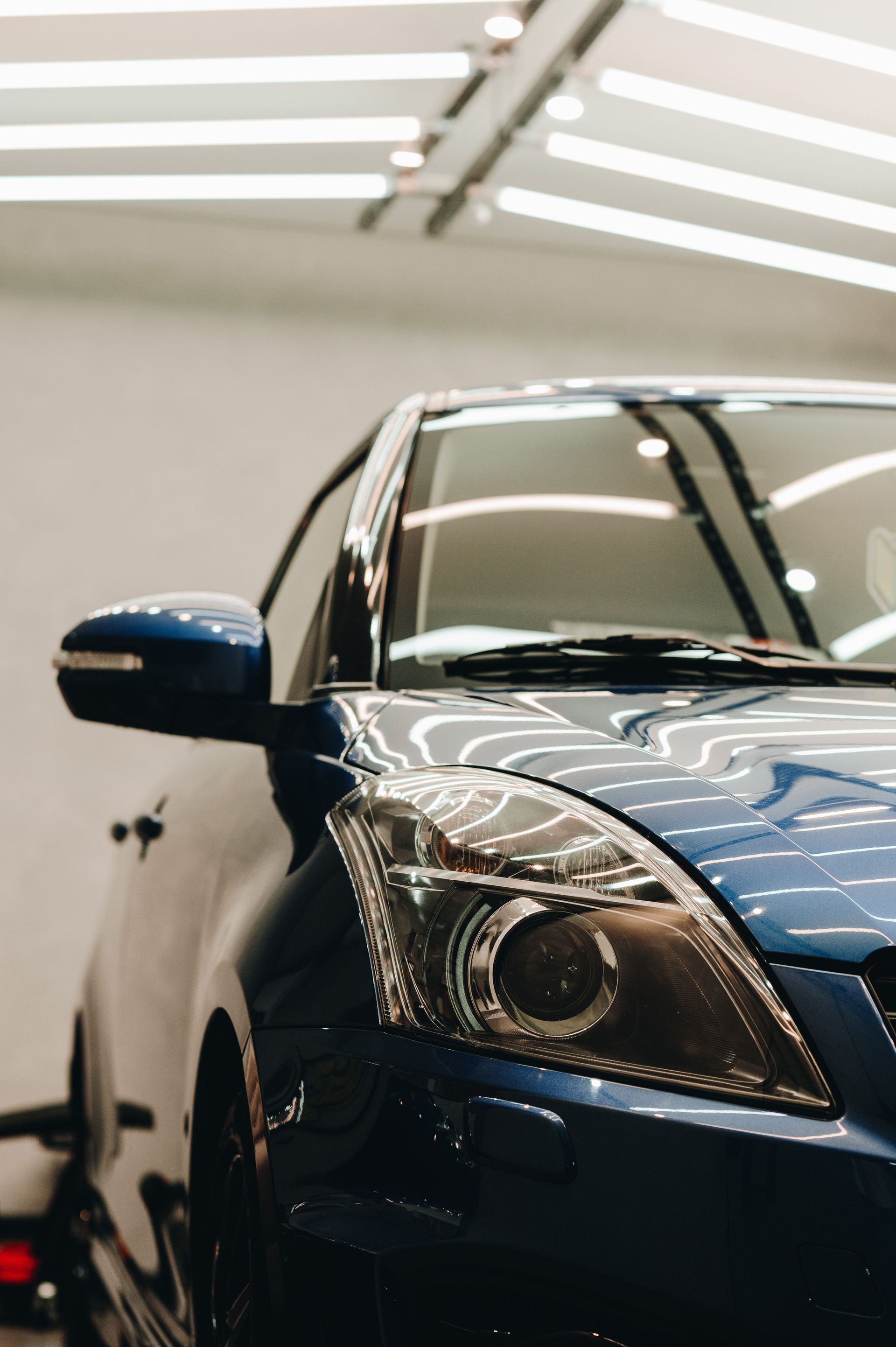 A blue car's headlight and side mirror showcased in a sleek indoor garage setting.